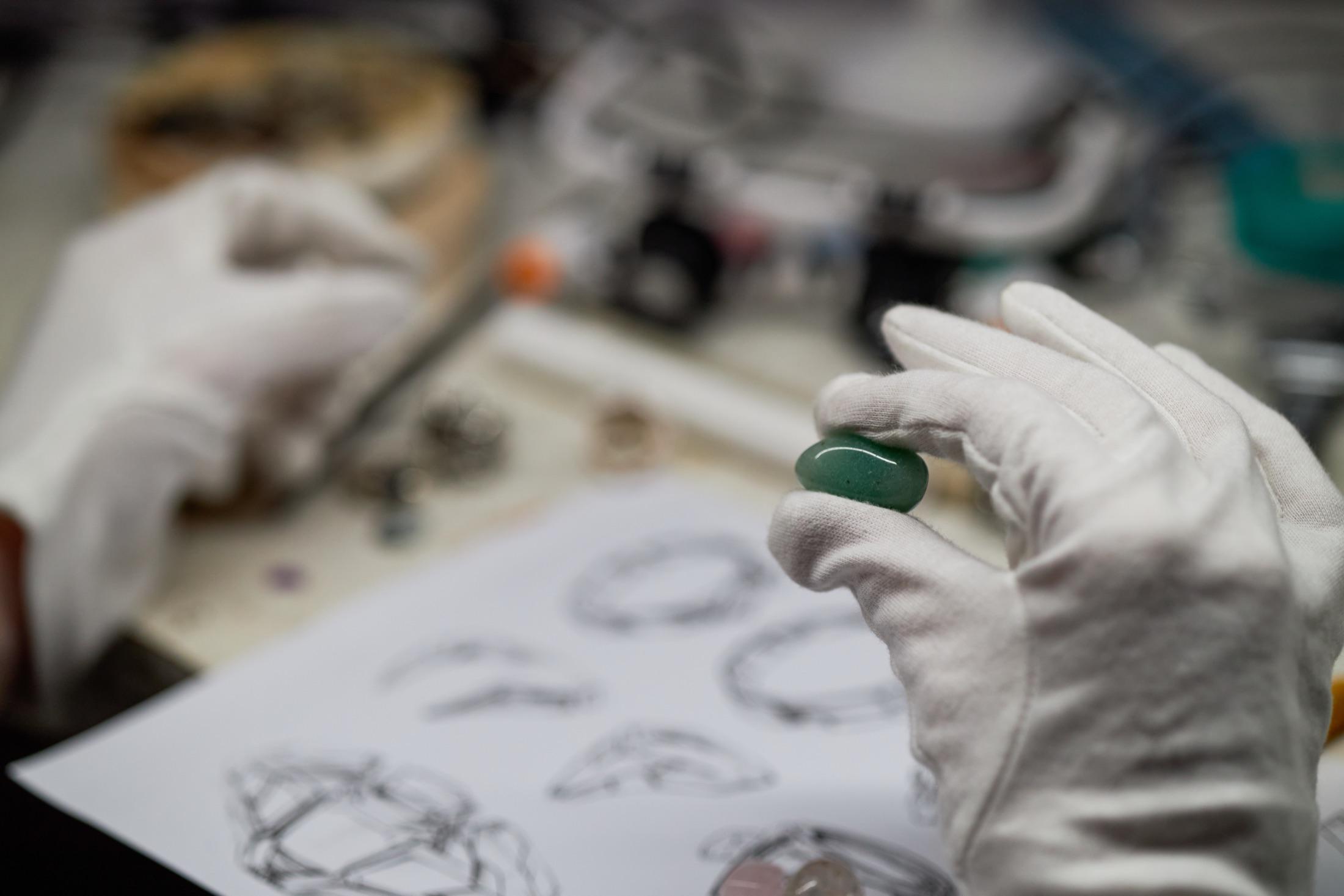 Gloved hand holding a natural emerald over jewelry design sketches