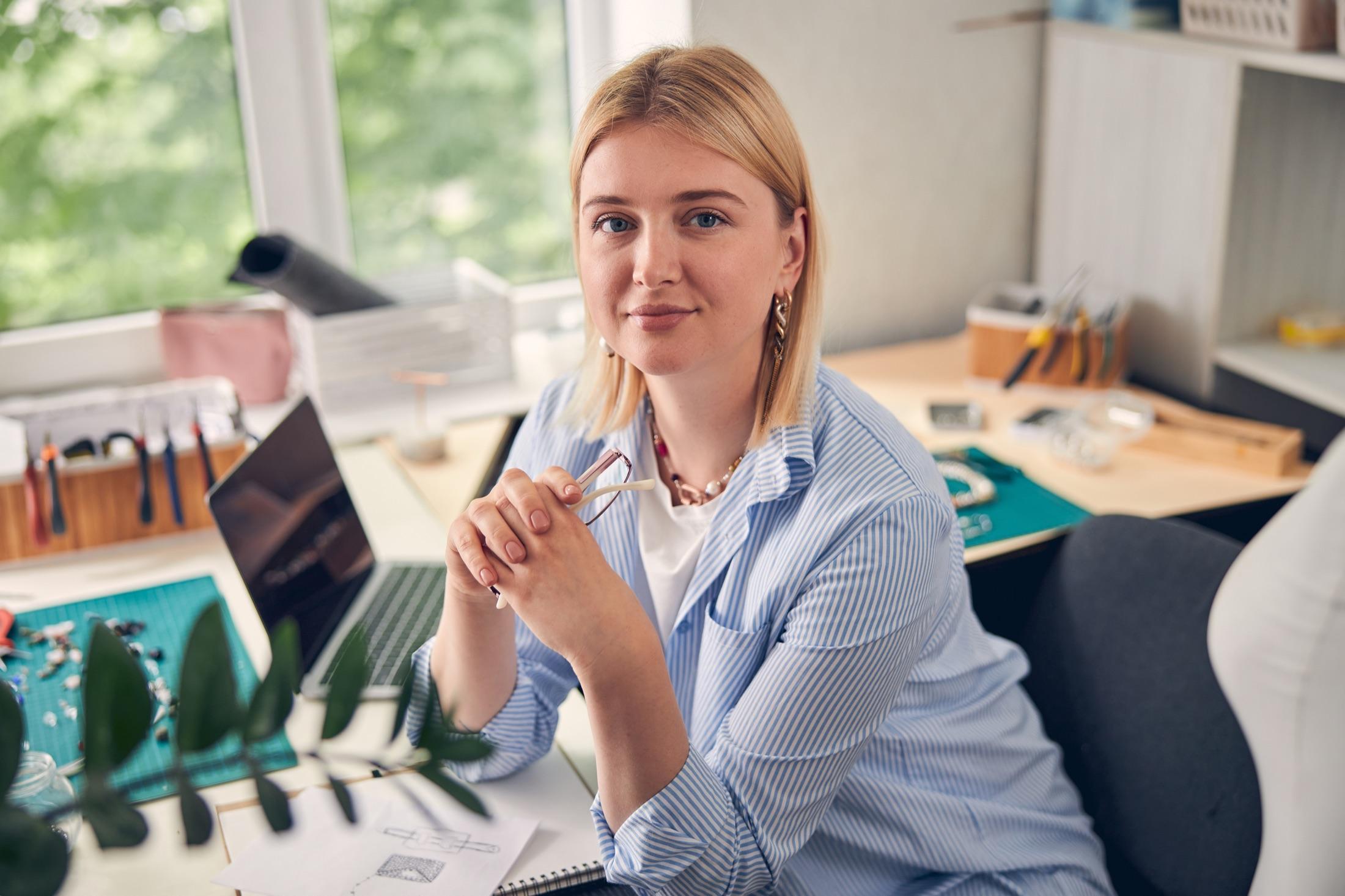 Jewelry designer at her desk with sketches, tools and a laptop, beginning a new project